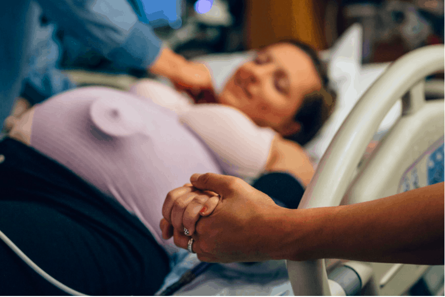Woman waiting in labour on hospital bed holding partner's hand
